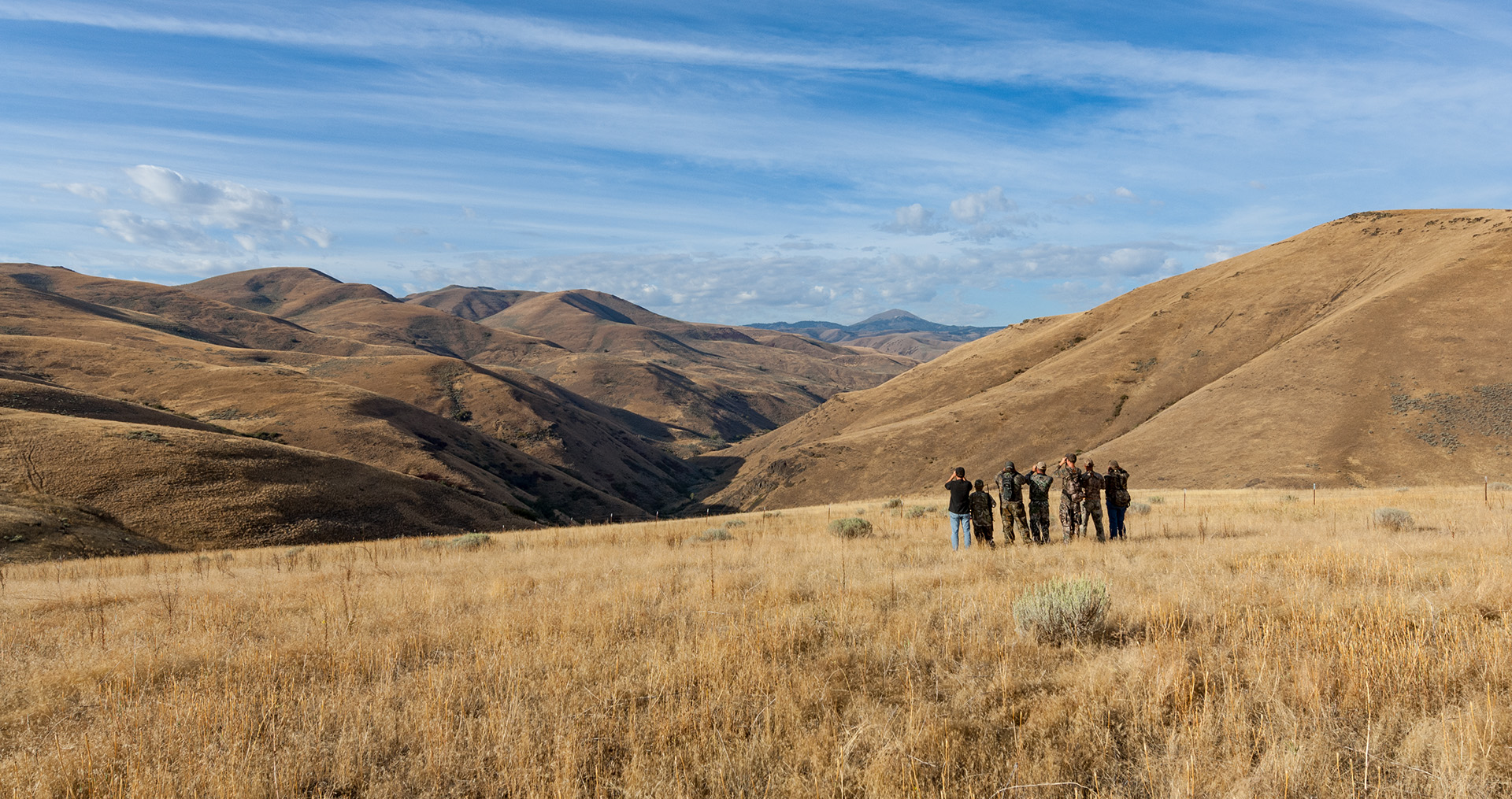 men standing in a field looking into a valley with binoculars