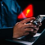 Person with a computer and phone and a warning sign near the phone