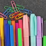 colorful illustration showing several colors of pens, pencils, paper clips and other school supplies.