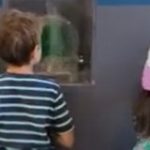 Two young children facing away from the camera, operating a model of a hydropower plant illuminating a large wall display.
