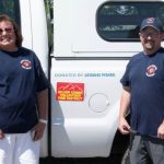 A group of five people standing in front of a white pickup truck with a camper shell on it. They are smiling and looking at the camera.