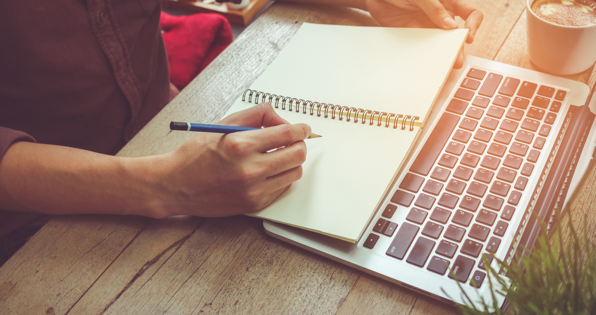 person writing notes in a notepad with their laptop in front of them